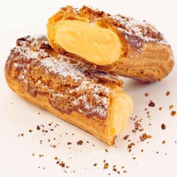 The image shows a pastry filled with cream, likely dusted with powdered sugar. It falls under the categories of food, snacks, and desserts, typically associated with bakeries. This baked good could be enjoyed as a finger food or part of a larger cuisine presentation indoors.