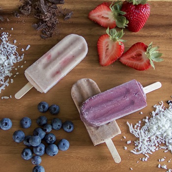 A group of colorful popsicles is displayed, featuring strawberries and coconut shavings on their surfaces. The scene includes fresh strawberries, emphasizing a fruity and refreshing theme. It captures a delightful food moment, ideal for warm days or special occasions.