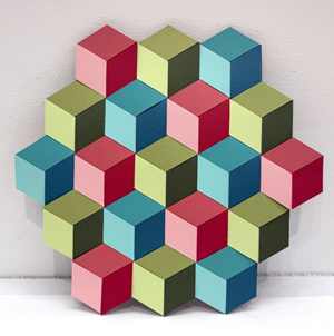 The image displays a geometric arrangement of three-dimensional cubes, presented in a hexagonal pattern on a textured white background. The cubes appear to be made of paper or cardstock, with a matte finish and visible paper grain. They are arranged in concentric layers, with the widest layer forming a hexagonal outline, and a single cube at the center.