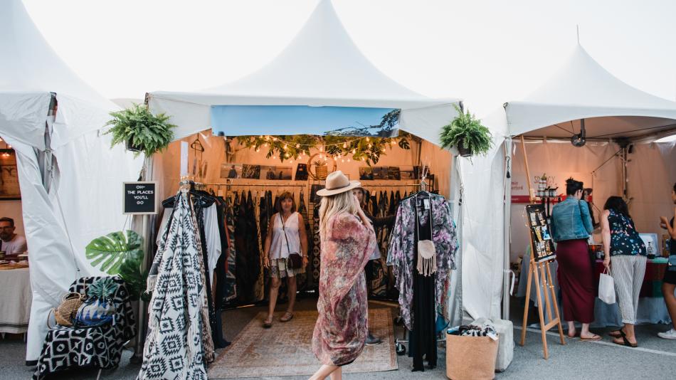 A woman strolls through a vibrant art market, exploring various tents filled with unique items.