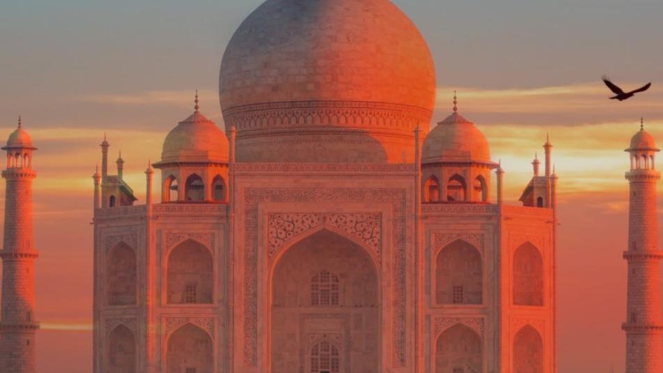  The photo shows a large building with a domed roof in the foreground, with the Taj Mahal in the background during sunset. It is a beautiful scene capturing the historic and architectural significance of the two structures.