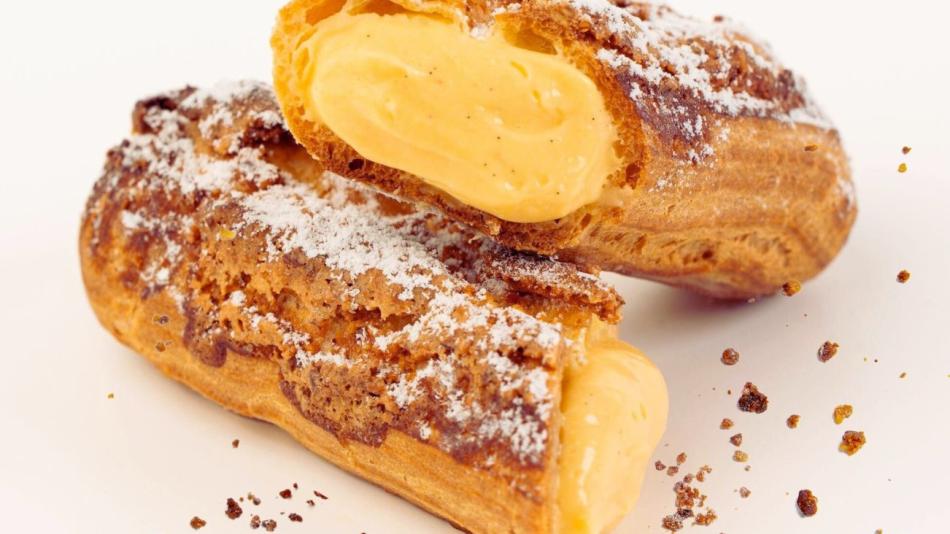 The image shows a pastry filled with cream, likely dusted with powdered sugar. It falls under the categories of food, snacks, and desserts, typically associated with bakeries. This baked good could be enjoyed as a finger food or part of a larger cuisine presentation indoors.