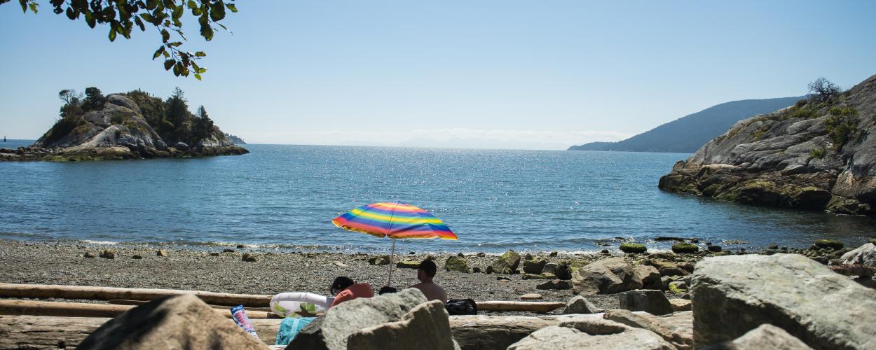 A colourful umbrella rests on a rocky beach on a clear sunny day.
