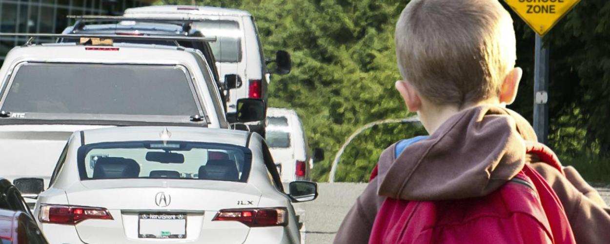 Child with backpack on right side of image and a row of cars to the left of child