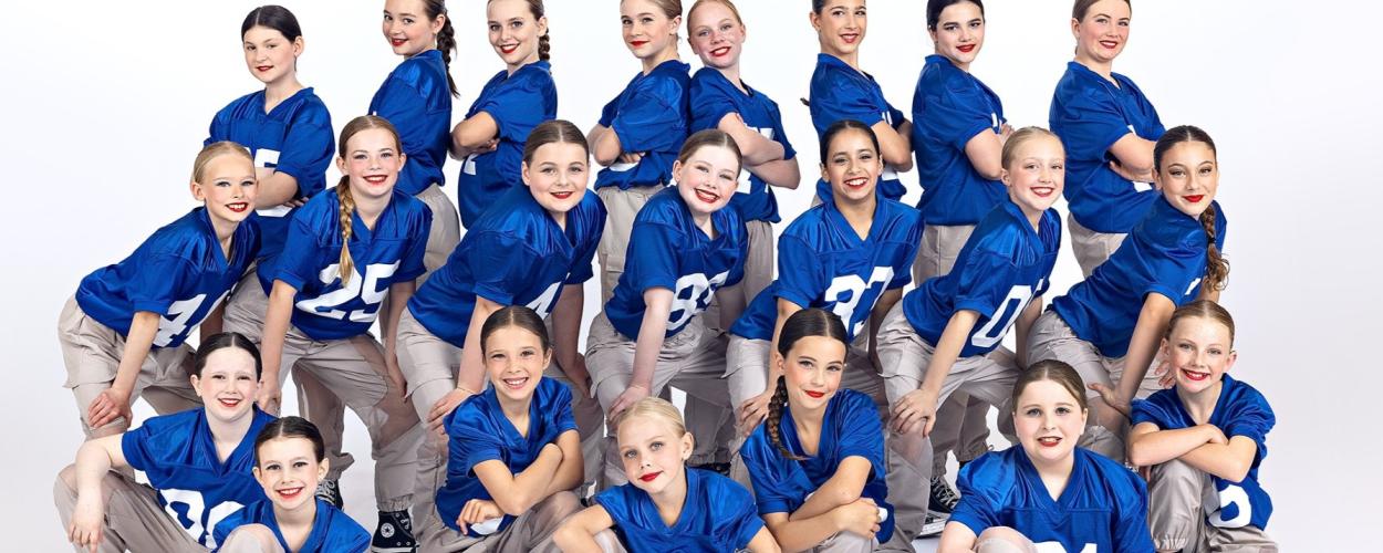 A group of young girls in blue uniforms, dancing while wearing American football shirts, showcasing their energetic performance.