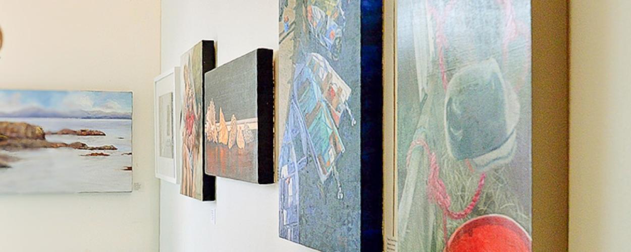 A woman gazes thoughtfully at various paintings displayed on a gallery wall.