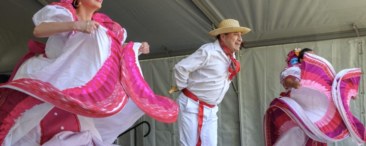 A lively group of individuals in colorful Mexican costumes joyfully dancing together in a festive atmosphere.