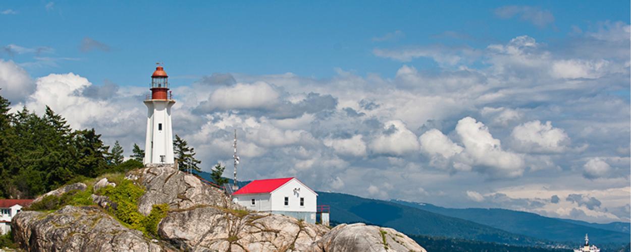 A red and white lighthouse sits on top of a large rocky hill.