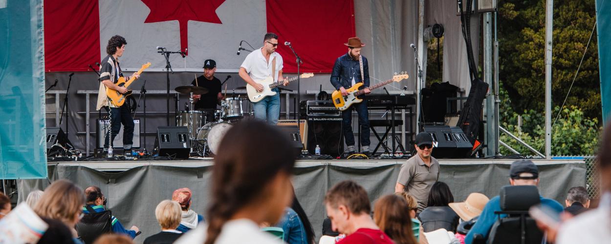 A band performs energetically on stage, with a prominent Canadian flag displayed in the background.
