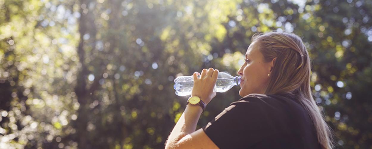 Woman outside on a sunny day drinking a bottle of water.