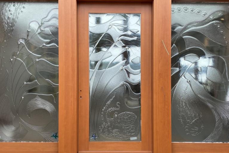 The image is a close-up of a window, showcasing details such as the building's architecture. It includes elements like a door and door handle, suggesting an entrance to an indoor space. The artwork or design around the window may also enhance its visual appeal.