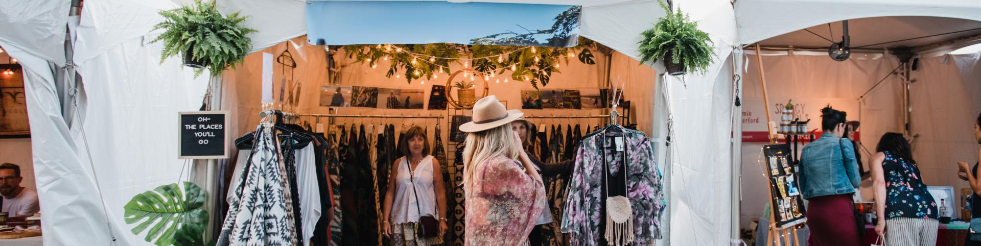 A woman strolls through a vibrant art market, exploring various tents filled with unique items.