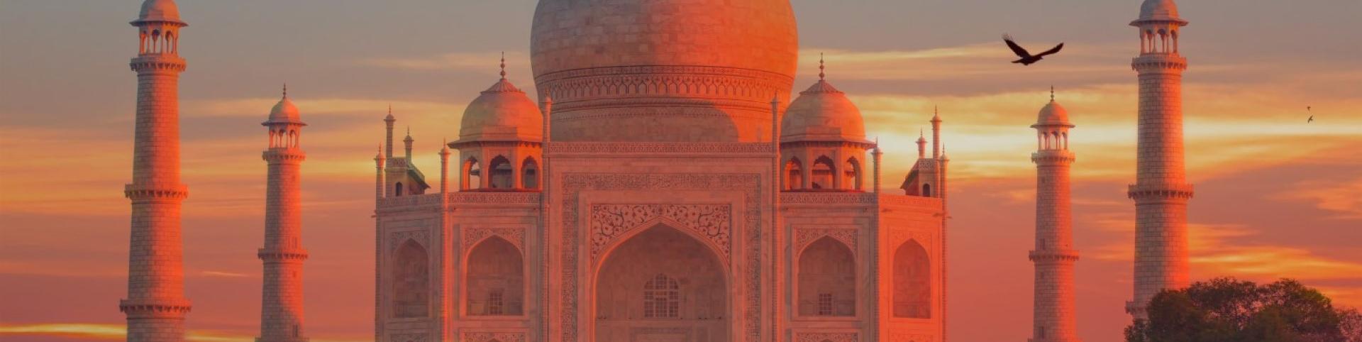 The photo shows a large building with a domed roof in the foreground, with the Taj Mahal in the background during sunset. It is a beautiful scene capturing the historic and architectural significance of the two structures.