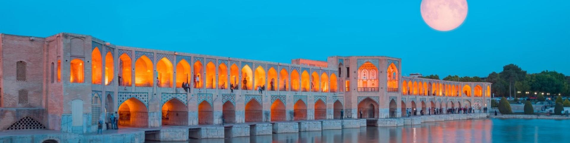  People can be seen resting in the Khaju Bridge in Iran. Key elements include the moon, water, building, sky, and reflection.