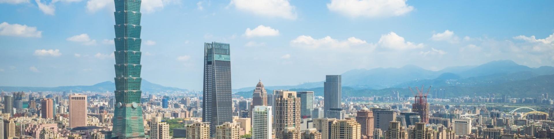 The photo is of a cityscape in Taiwan featuring tall buildings against a backdrop of clouds and sky. The urban area includes skyscrapers and tower blocks, creating a metropolitan landscape.