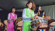 A group of women dressed in traditional attire joyfully playing drums together in a vibrant cultural celebration.